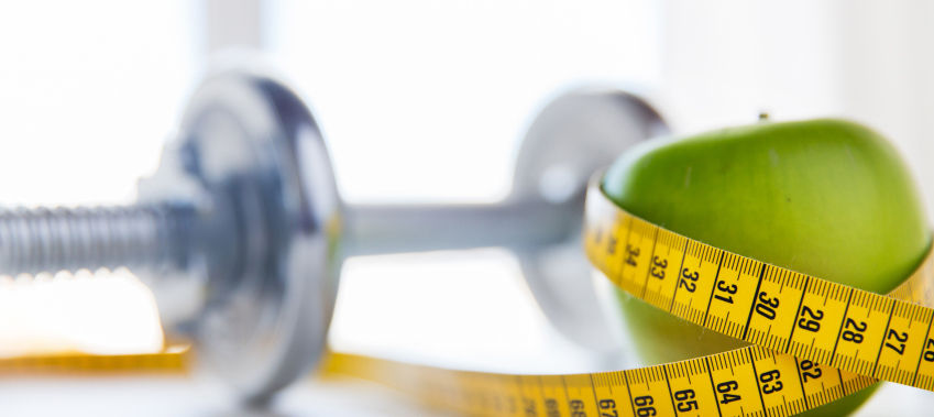 close up of dumbbell and apple with measuring tape