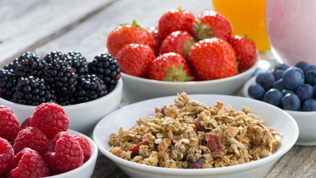 Strawberries, blueberries, blackberries, cherries and oatmeal in bowls on a wood table