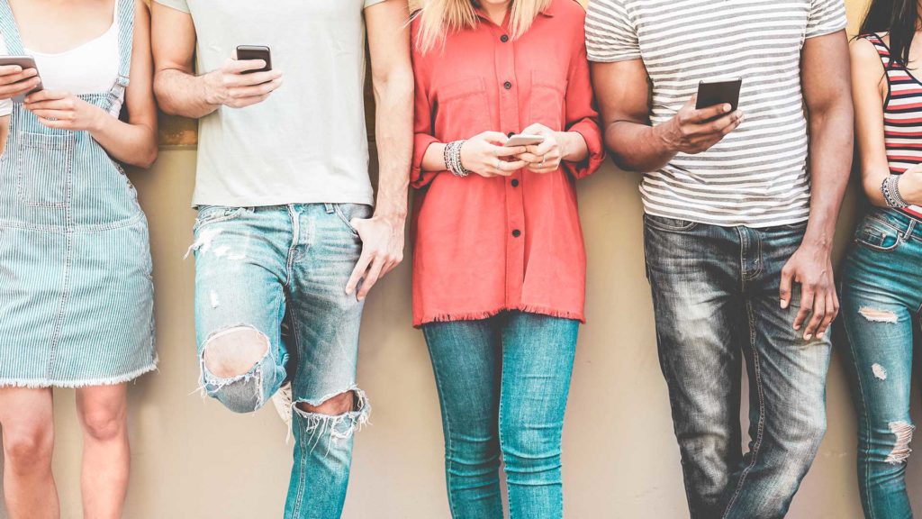 Group of people standing against a wall and using their cell phones
