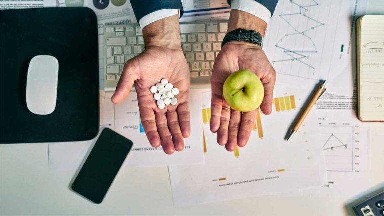 Person holding an apple in their left hand and medicine in right hand